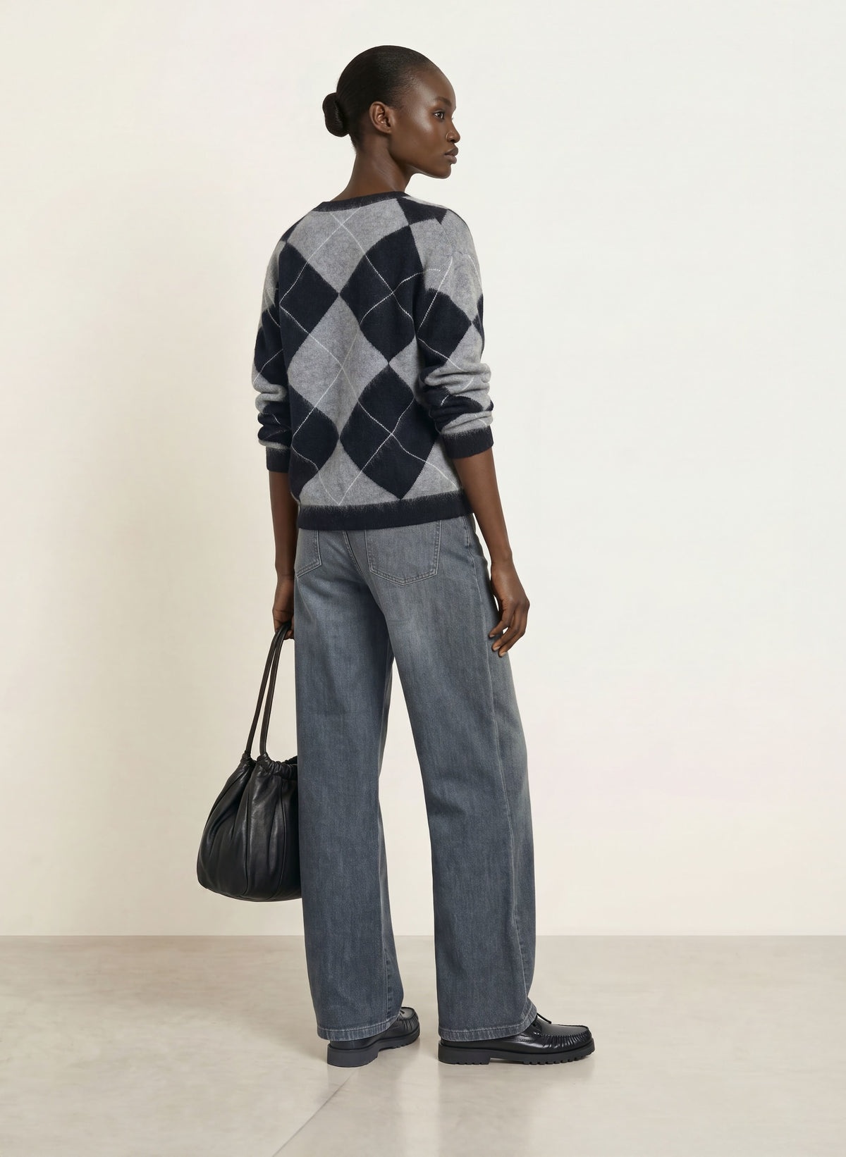 Wide-leg grey washed jeans styled with argyle sweater and black loafers, rear view