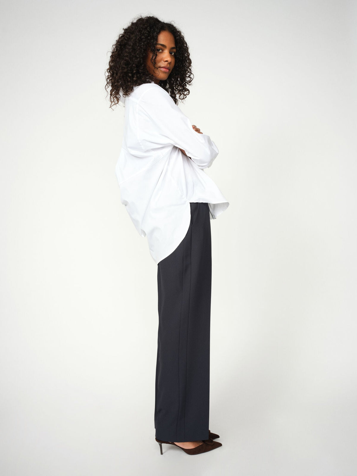 Model wearing Mos Mosh Bai Miley black wide-leg trousers with white oversized shirt, side view