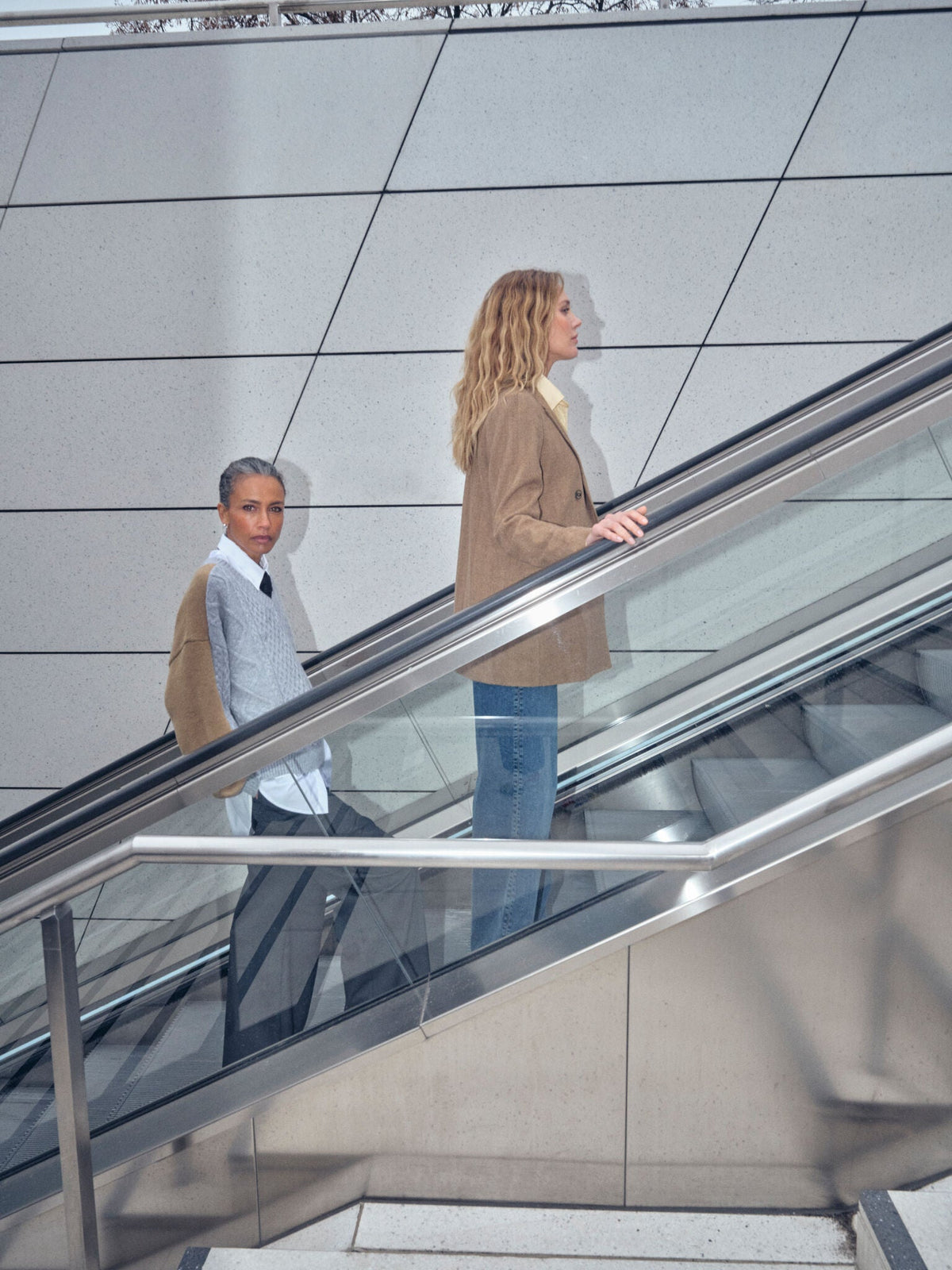 Two women on escalator wearing Mos Mosh Bethie Case Blazer in dark camel with jeans