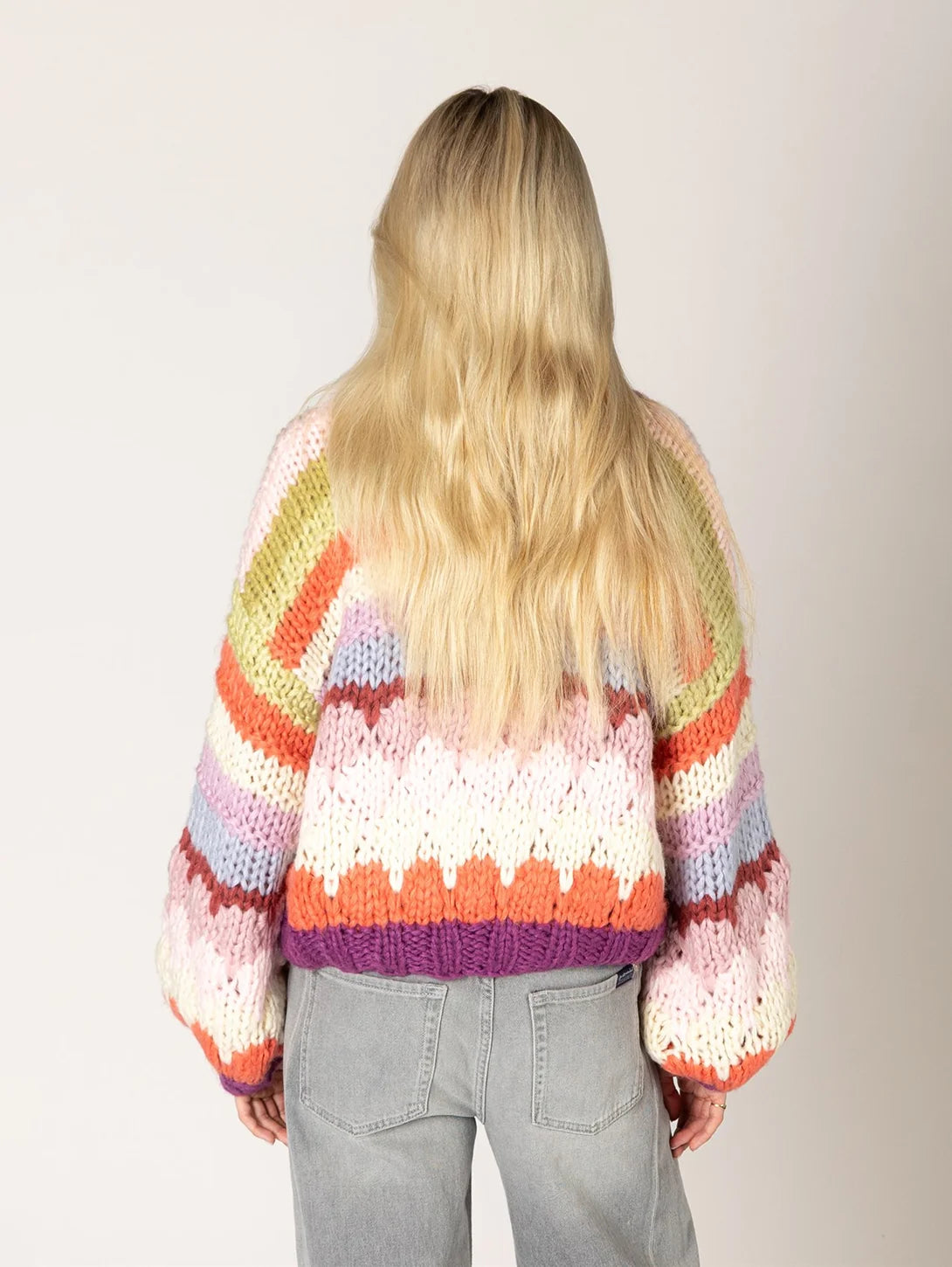 Chunky knit striped sweater in multicolor zigzag pattern with purple hem, back view