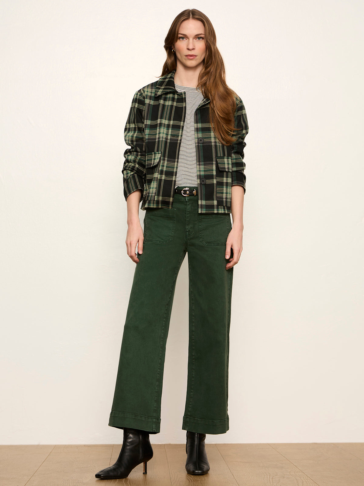 Model wearing Sanctuary Avid Plaid Jacket in evergreen plaid over striped tee and green pants.