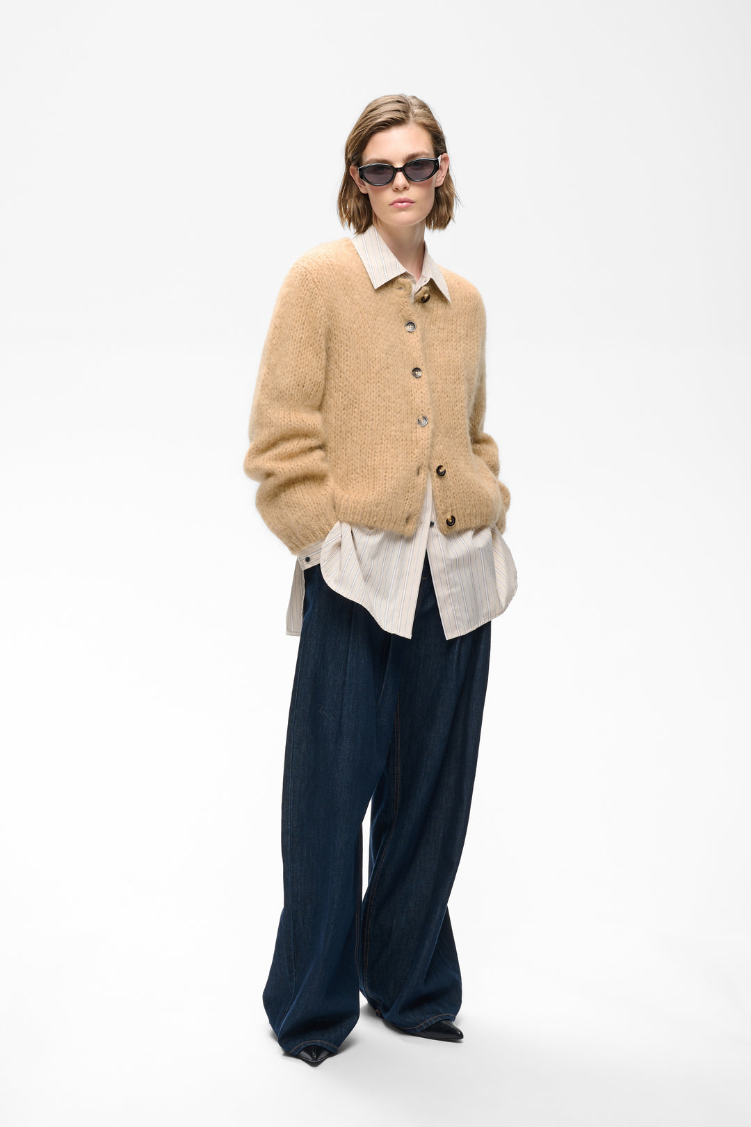 Camel chunky knit cardigan with button front, worn over striped shirt with wide-leg jeans.