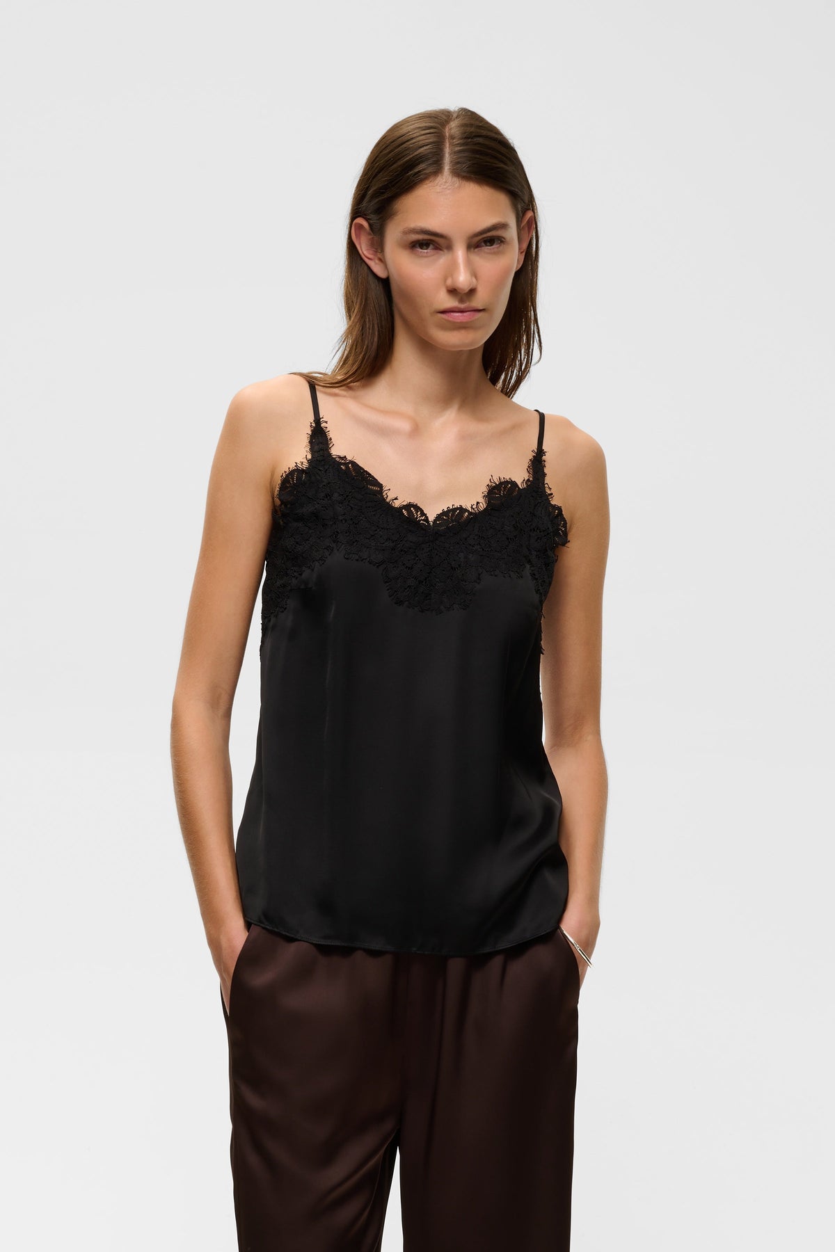 Model wearing black satin camisole with lace trim neckline and thin straps