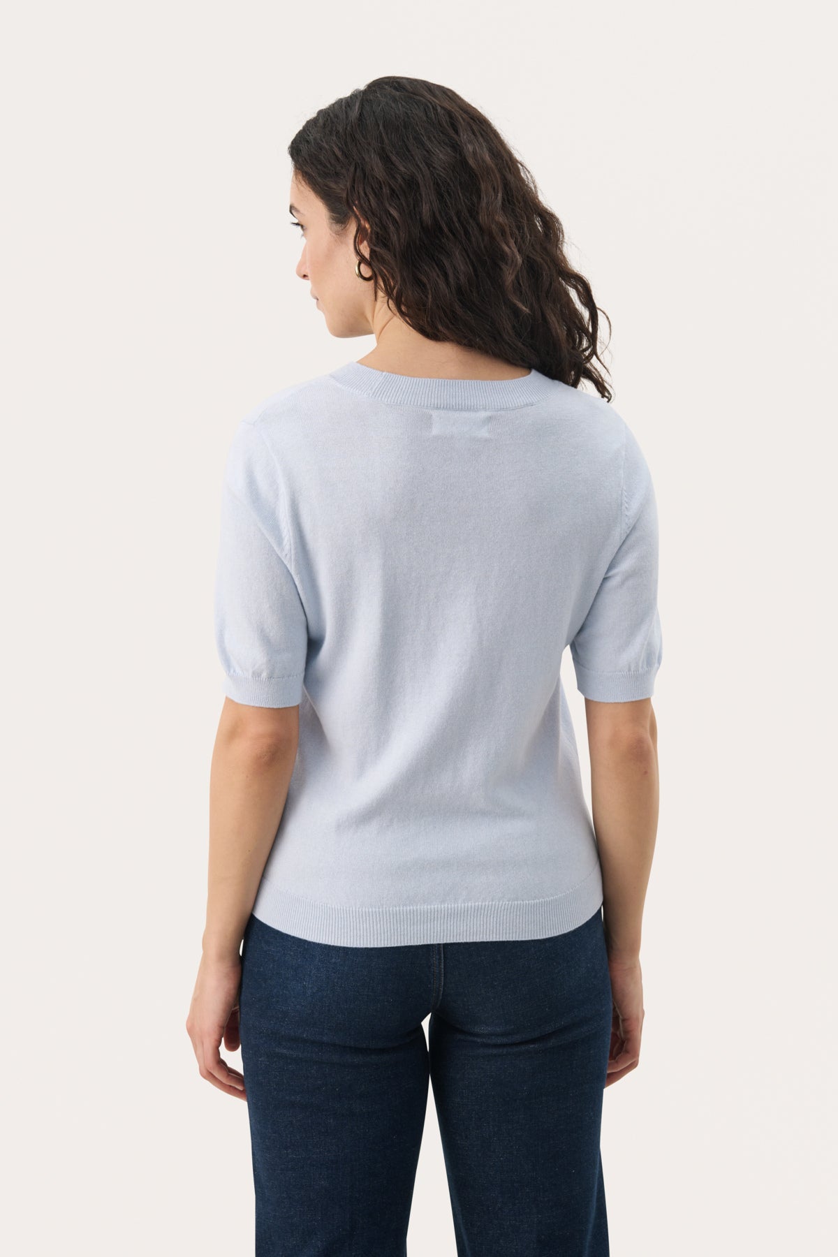 Back view of woman wearing Part Two Everlotta light blue short-sleeve knit pullover with dark jeans.