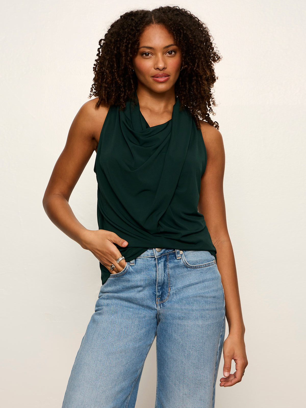 Woman wearing Sanctuary Nora Draped Tank in forest green with light blue jeans