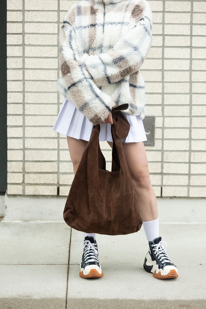 Brown suede knot tote bag held by model wearing white pleated skirt