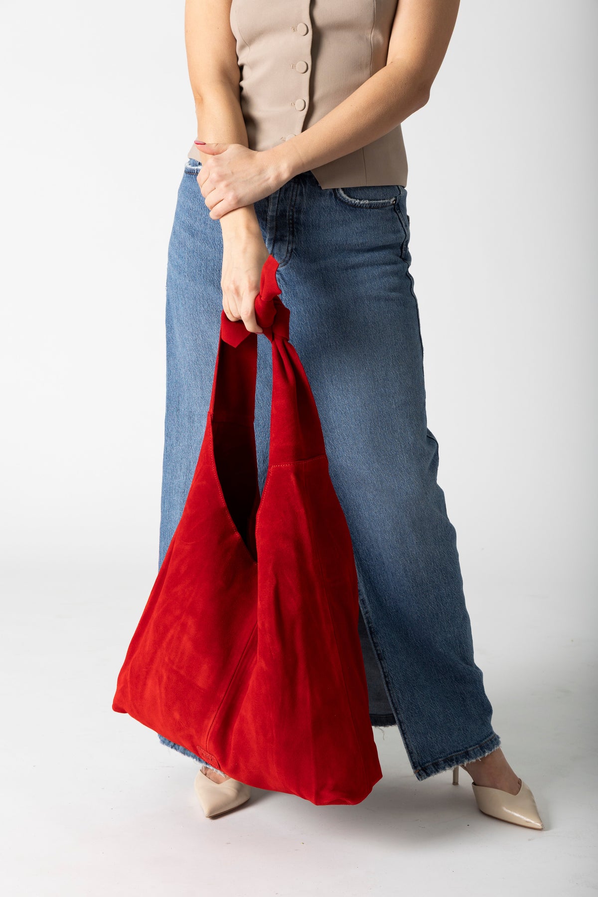 Model holding a red suede knot tote bag against a white background wearing jeans