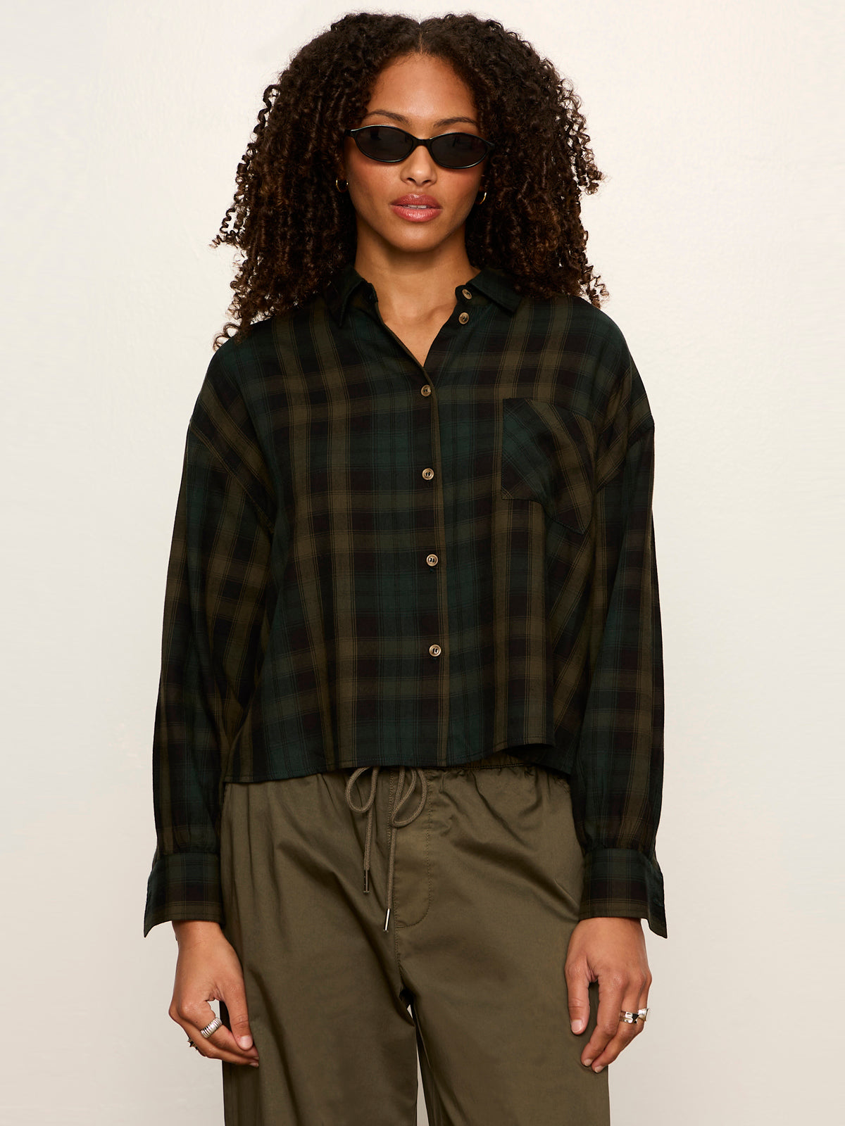 Model wearing Sanctuary Autumn Edit Flannel in Forest Plaid cropped button-down shirt with olive pants