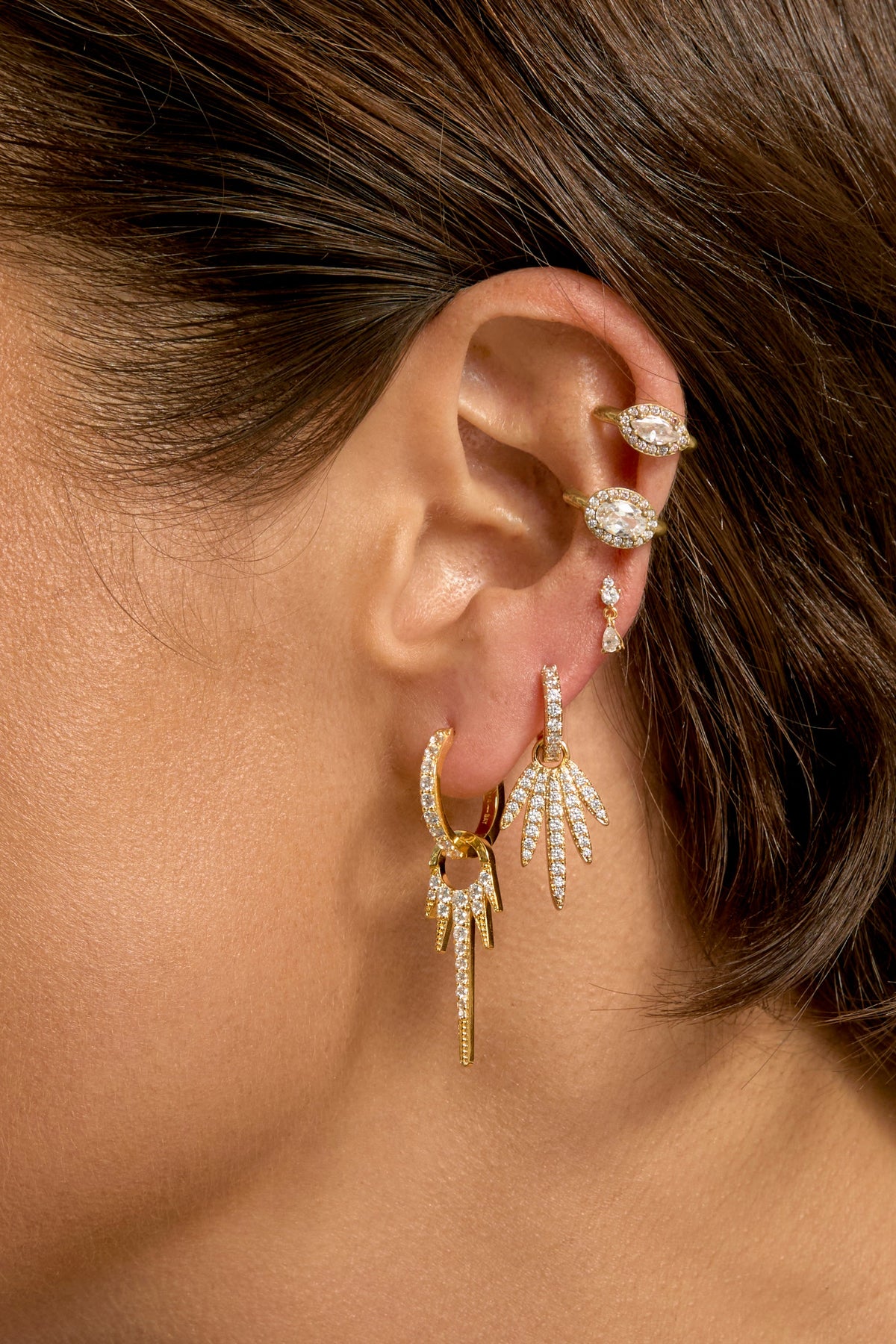 Gold crystal-encrusted FIRE earrings with dangling spike charms worn on model's ear