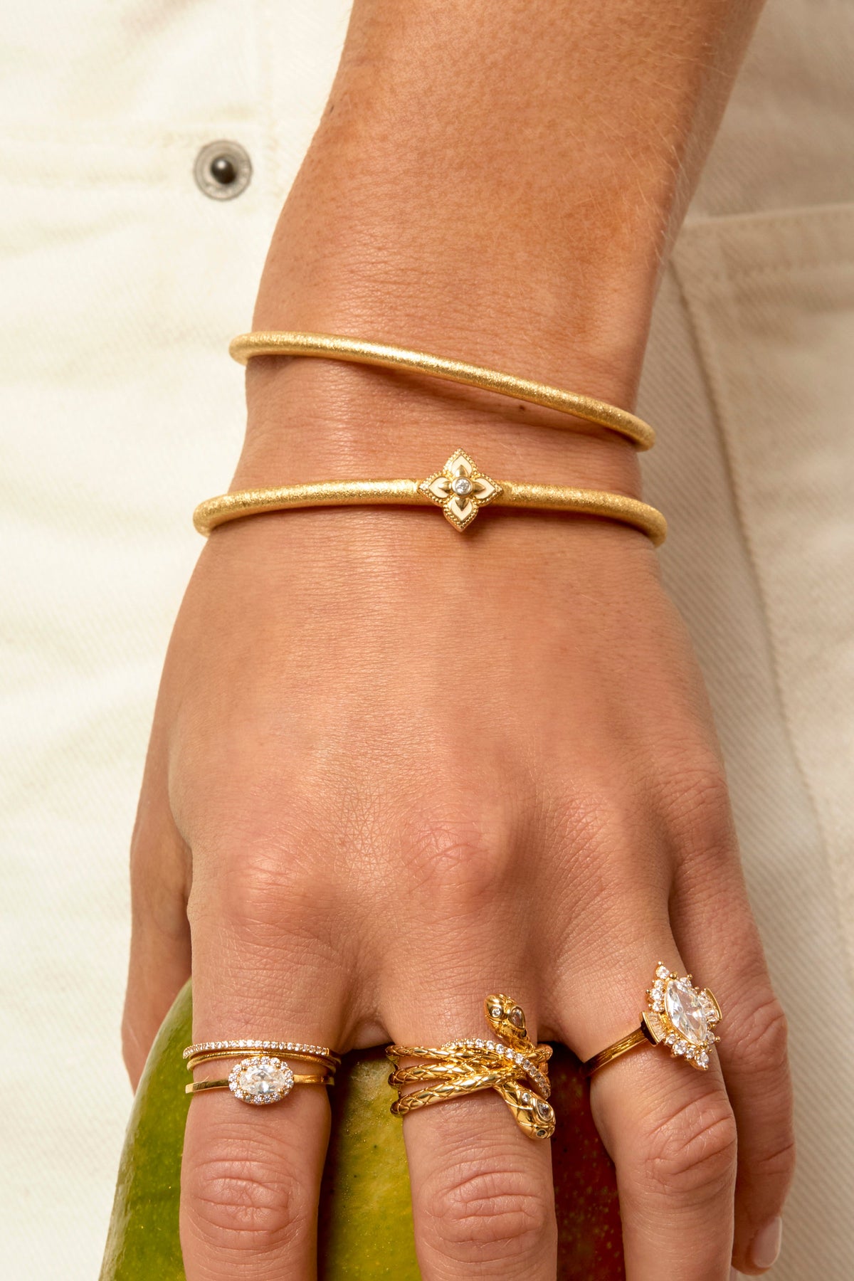 Gold White Lotus cuff bracelets stacked on wrist alongside gold rings holding mango