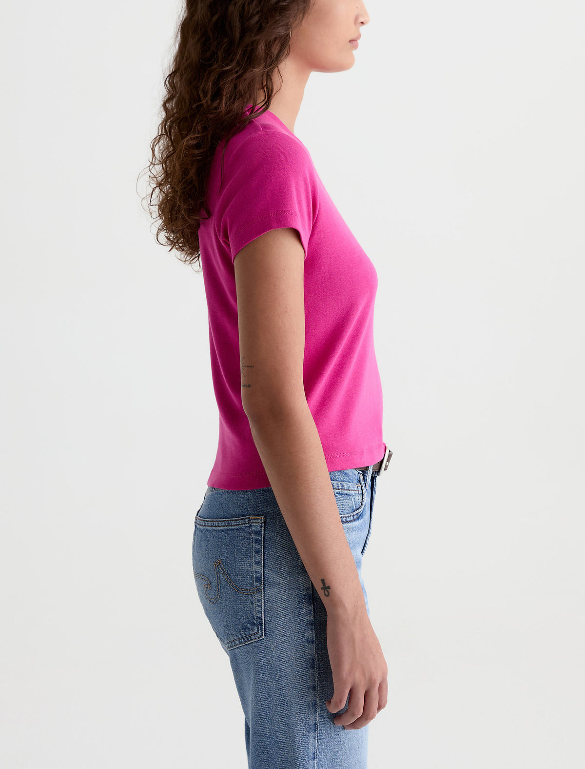 Side view of woman wearing AG Sadie Crew t-shirt in bright pink with blue jeans