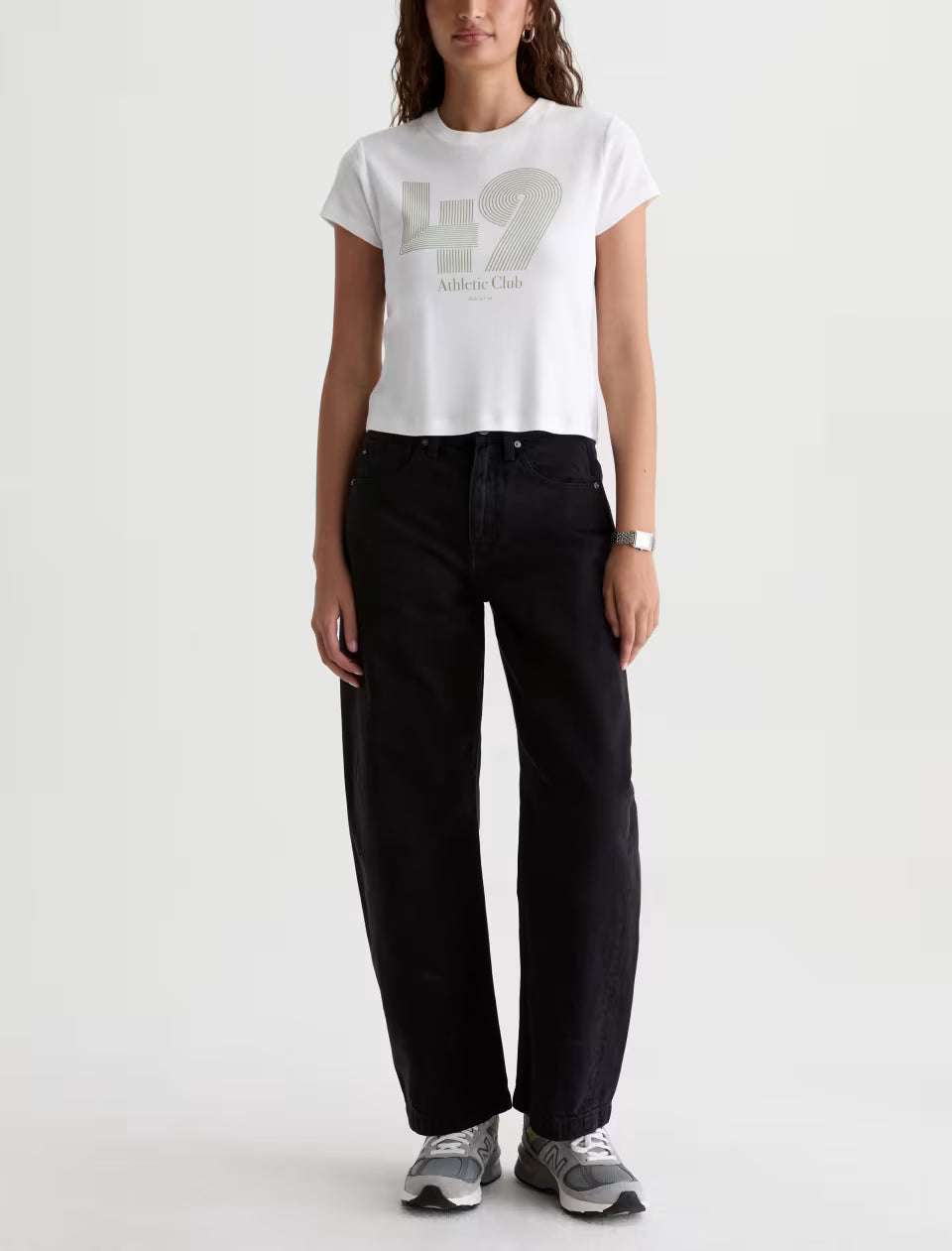 Woman wearing black wide-leg jeans with white cropped graphic tee and gray sneakers