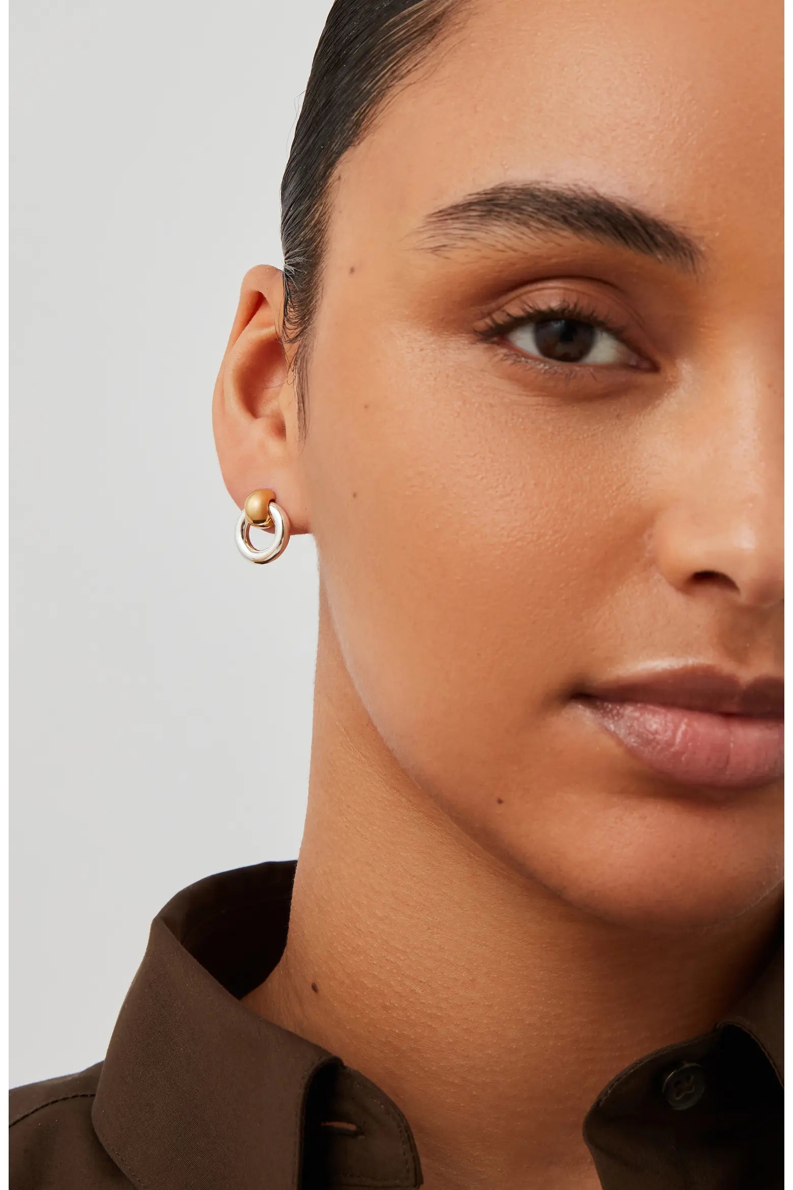 Gold and silver two-tone hoop earrings worn on the ear, featuring a rounded gold accent.
