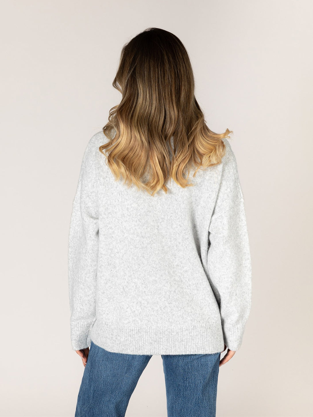 Back view of model wearing light ash gray crew neck knit sweater with blue jeans