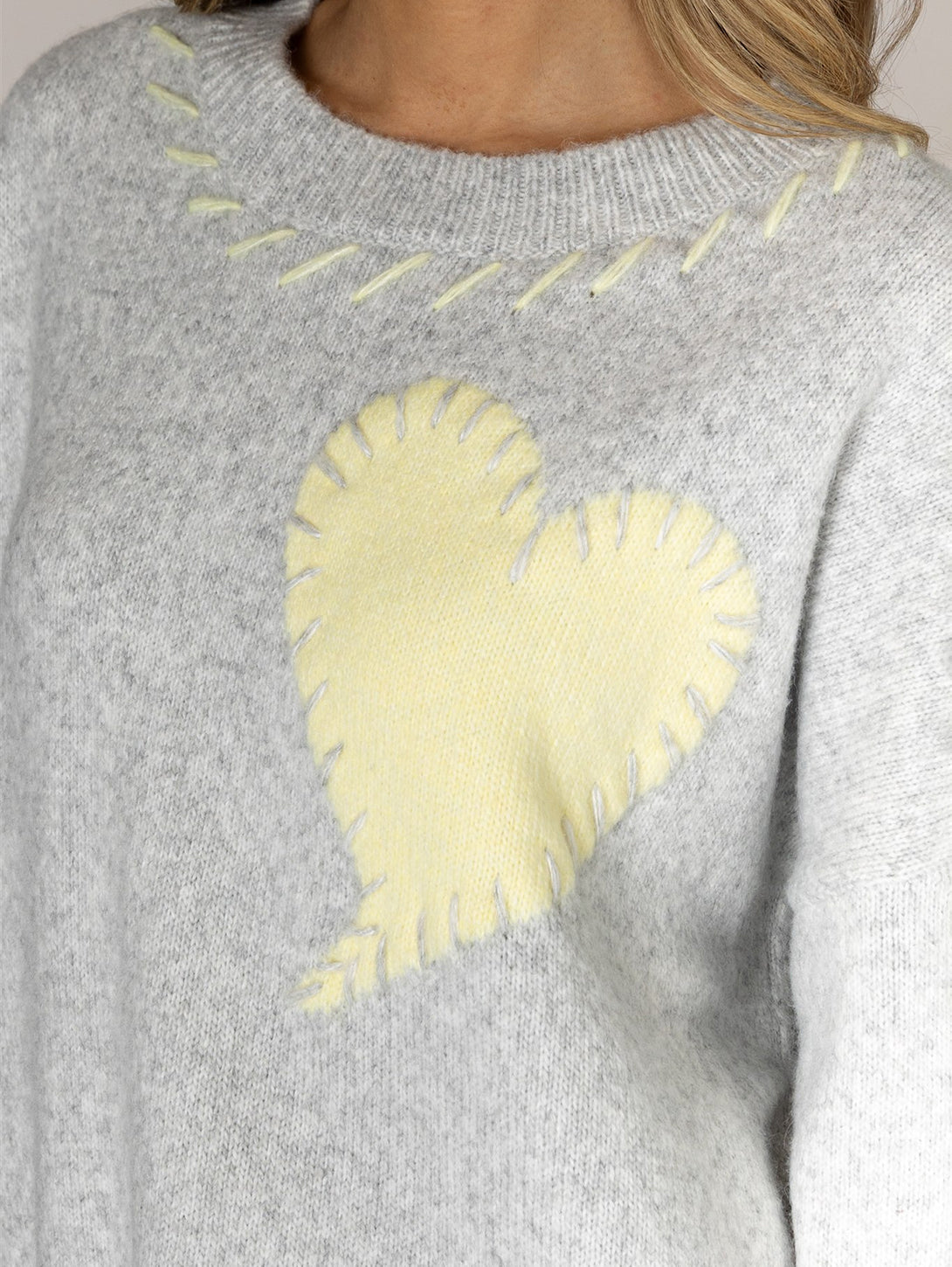 Close-up detail of gray knit sweater with yellow heart appliqué and whipstitch embroidery