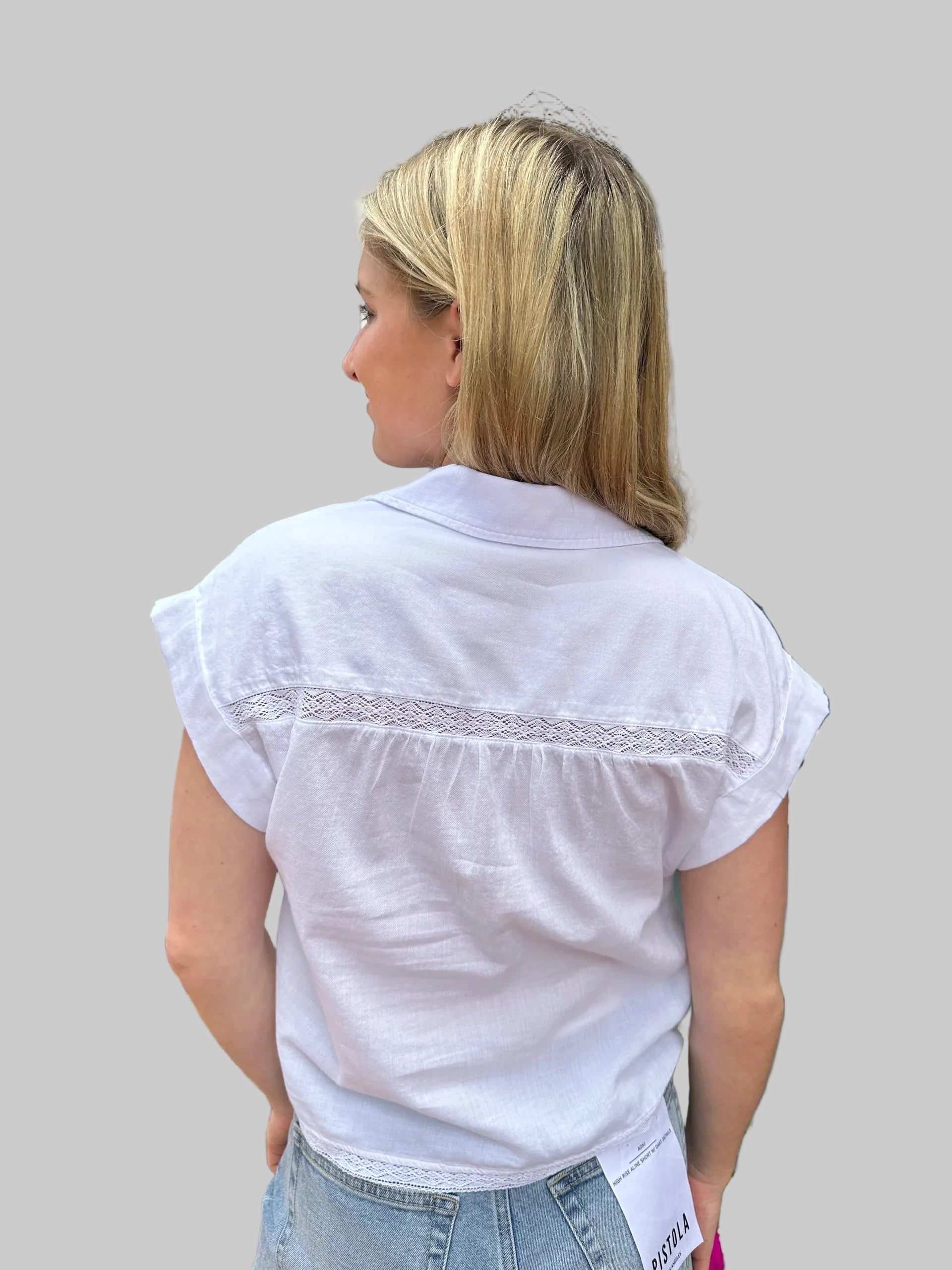 White cap sleeve shirt with lace trim detail and ruffle shoulders, back view