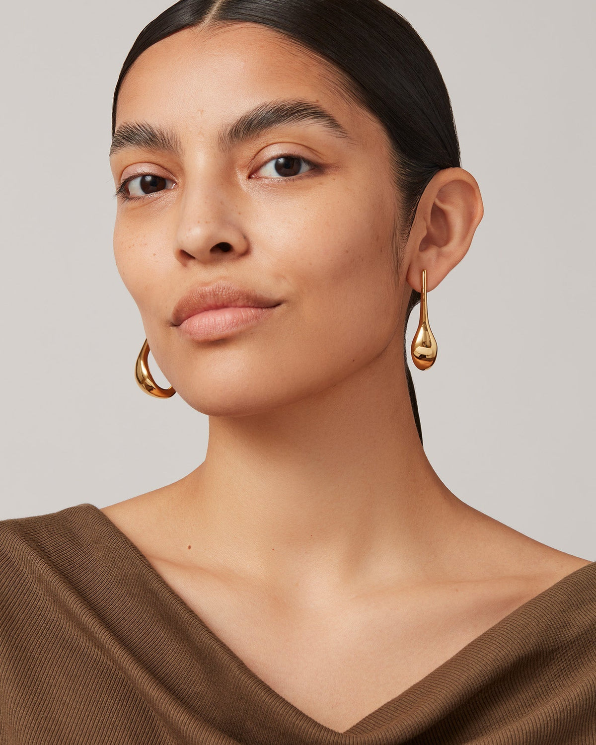Model wearing Jenny Bird Egret Hoops in tarnished gold, shown on both ears from front view.