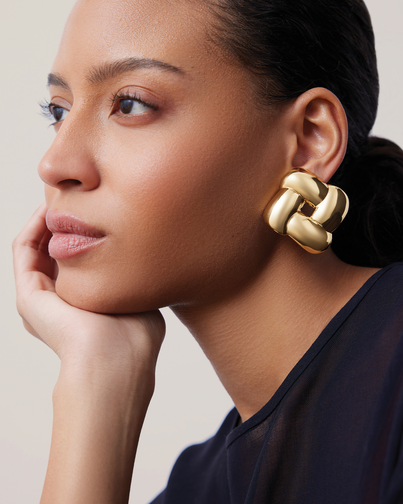 Model wearing Jenny Bird Gio Gold oversized sculptural knot statement earrings in profile view