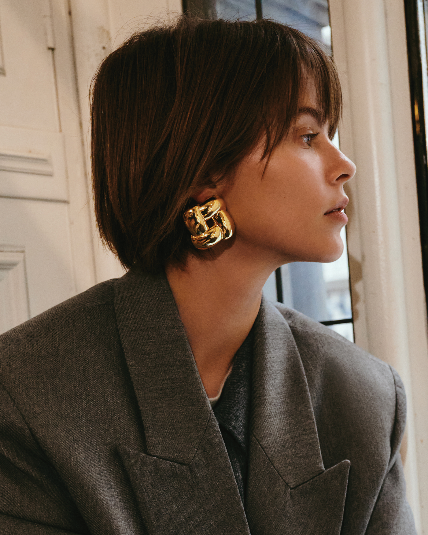 Model wearing large gold chunky square knot statement earring in profile view