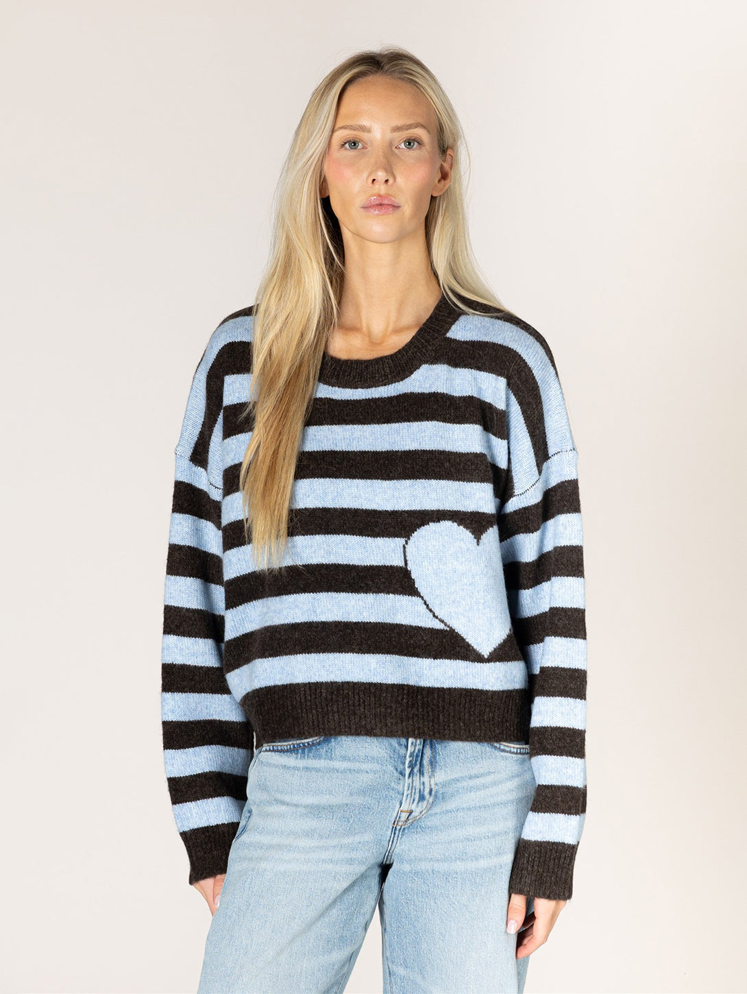 Model wearing brown and sky blue striped knit sweater with white heart motif on front
