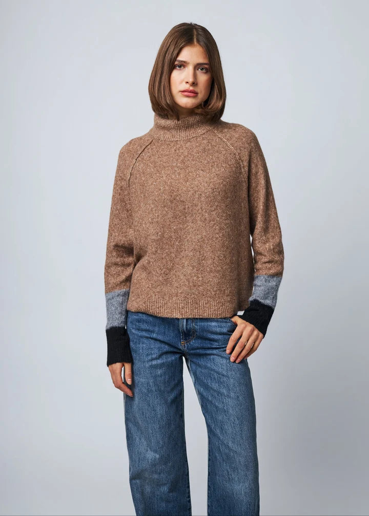 Brown turtleneck knit sweater with colorblock gray and black cuffs paired with blue jeans