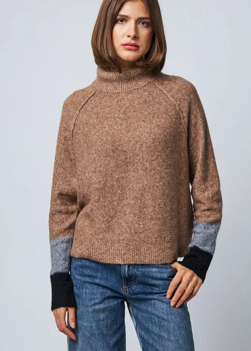 Camel turtleneck sweater with colorblock grey and black cuffs worn with blue jeans