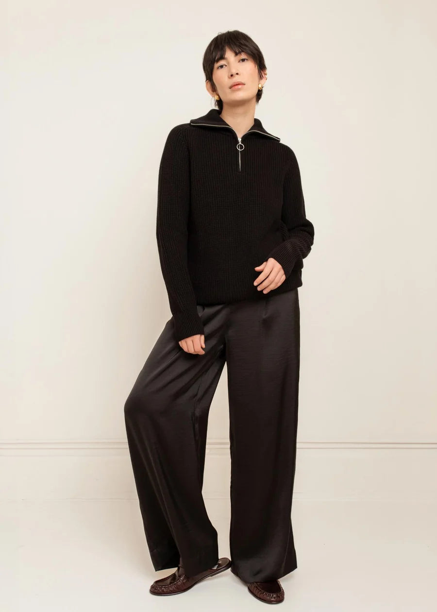 Black ribbed knit half-zip funnel neck sweater worn with wide-leg satin trousers