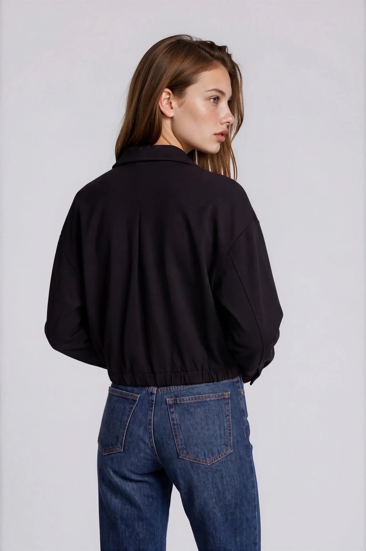 Black scuba bomber jacket with elastic hem and collar, worn with blue jeans