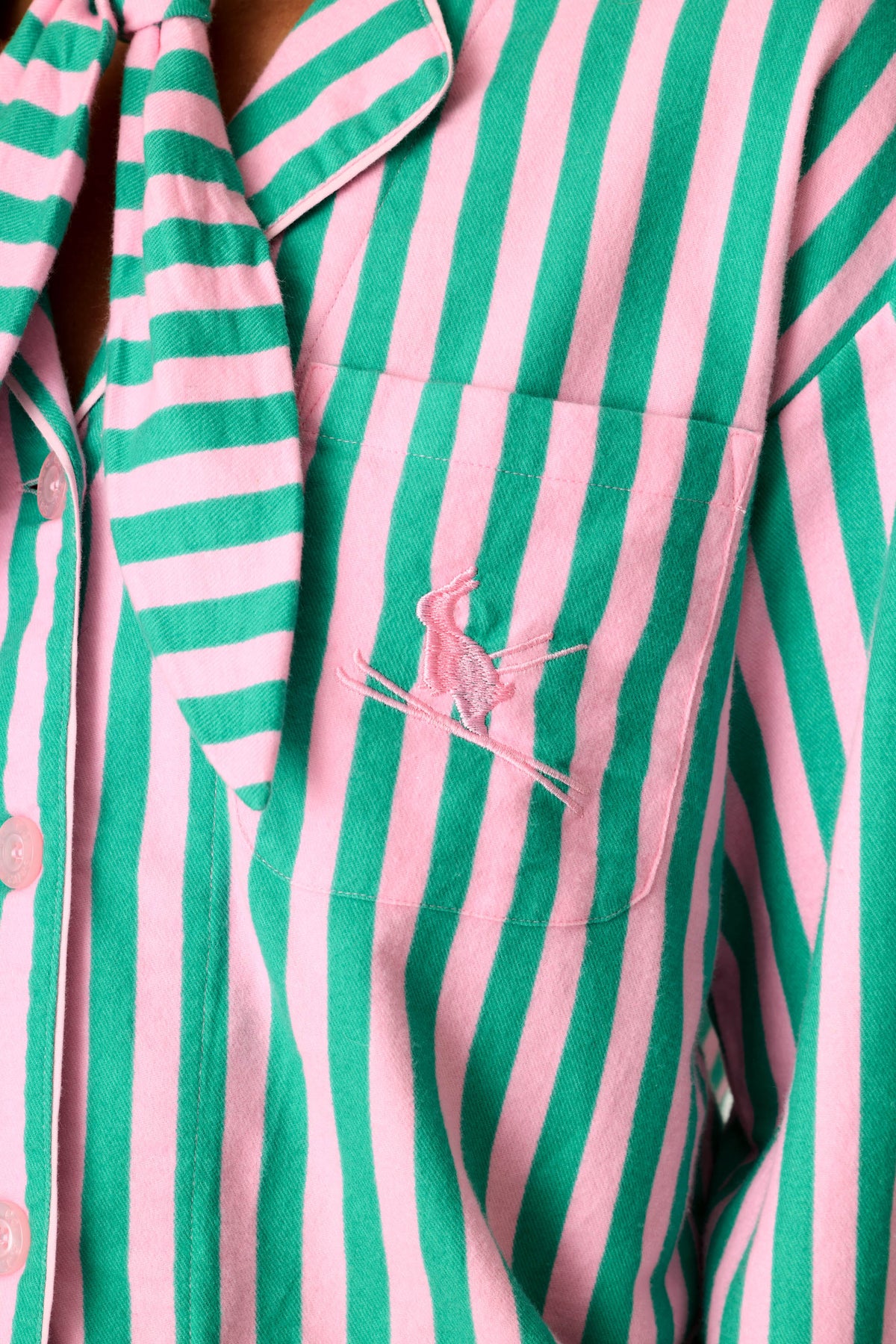 Close-up detail of pink and green striped PJ Salvage pajama shirt with embroidered skier logo on chest pocket