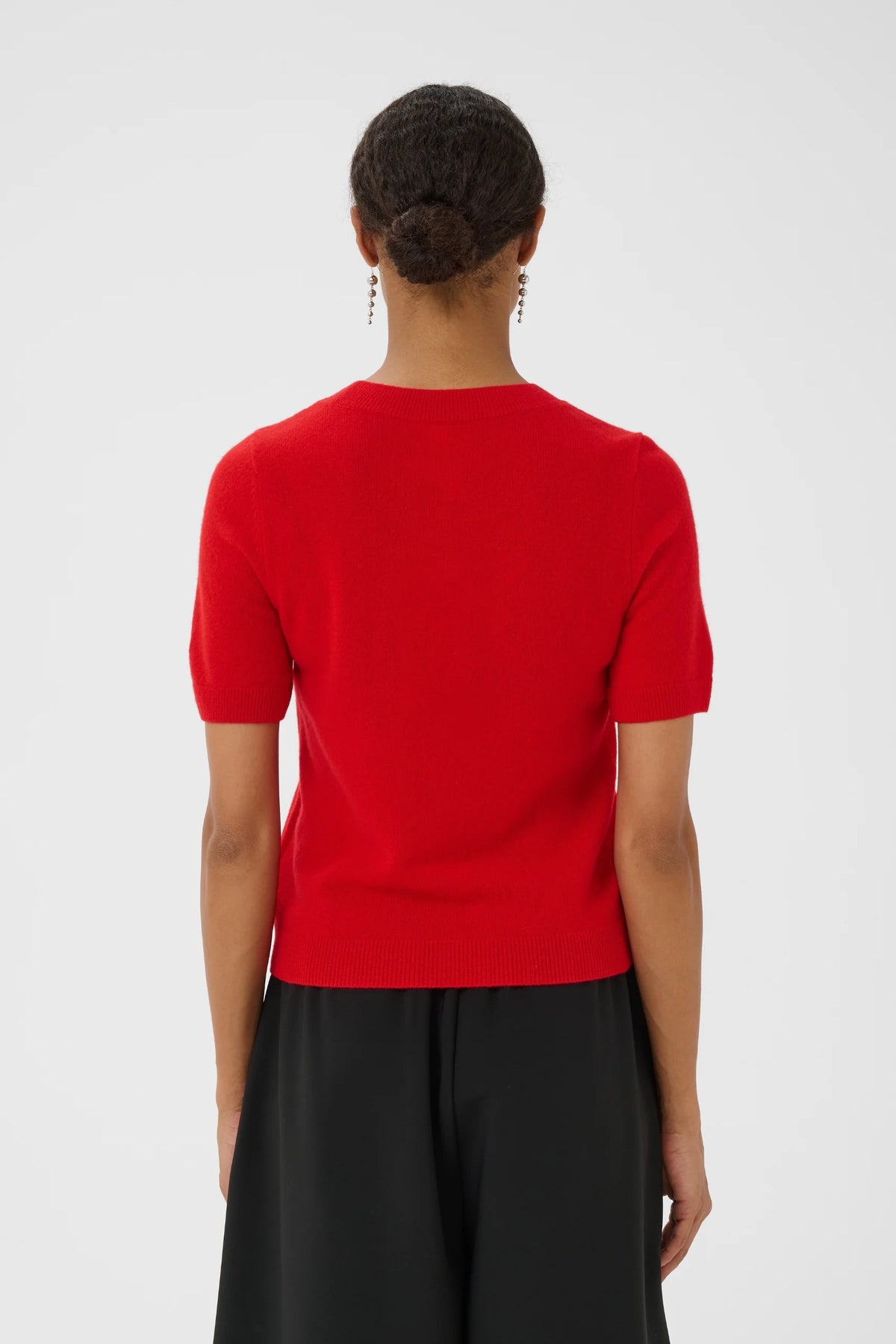Red short-sleeve knit pullover shown from the back, paired with black trousers.