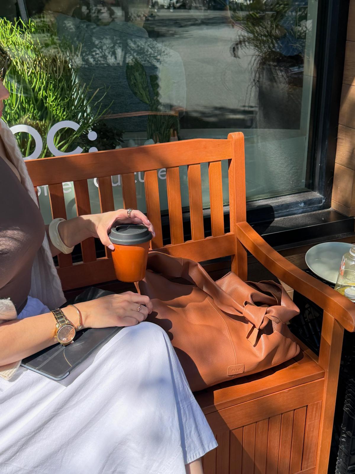 RISA Knot Tote Leather bag in tan, shown in lifestyle setting on wooden bench