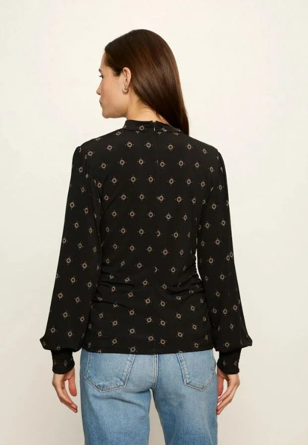 Black long-sleeve mock neck top with gold geometric print, worn with jeans