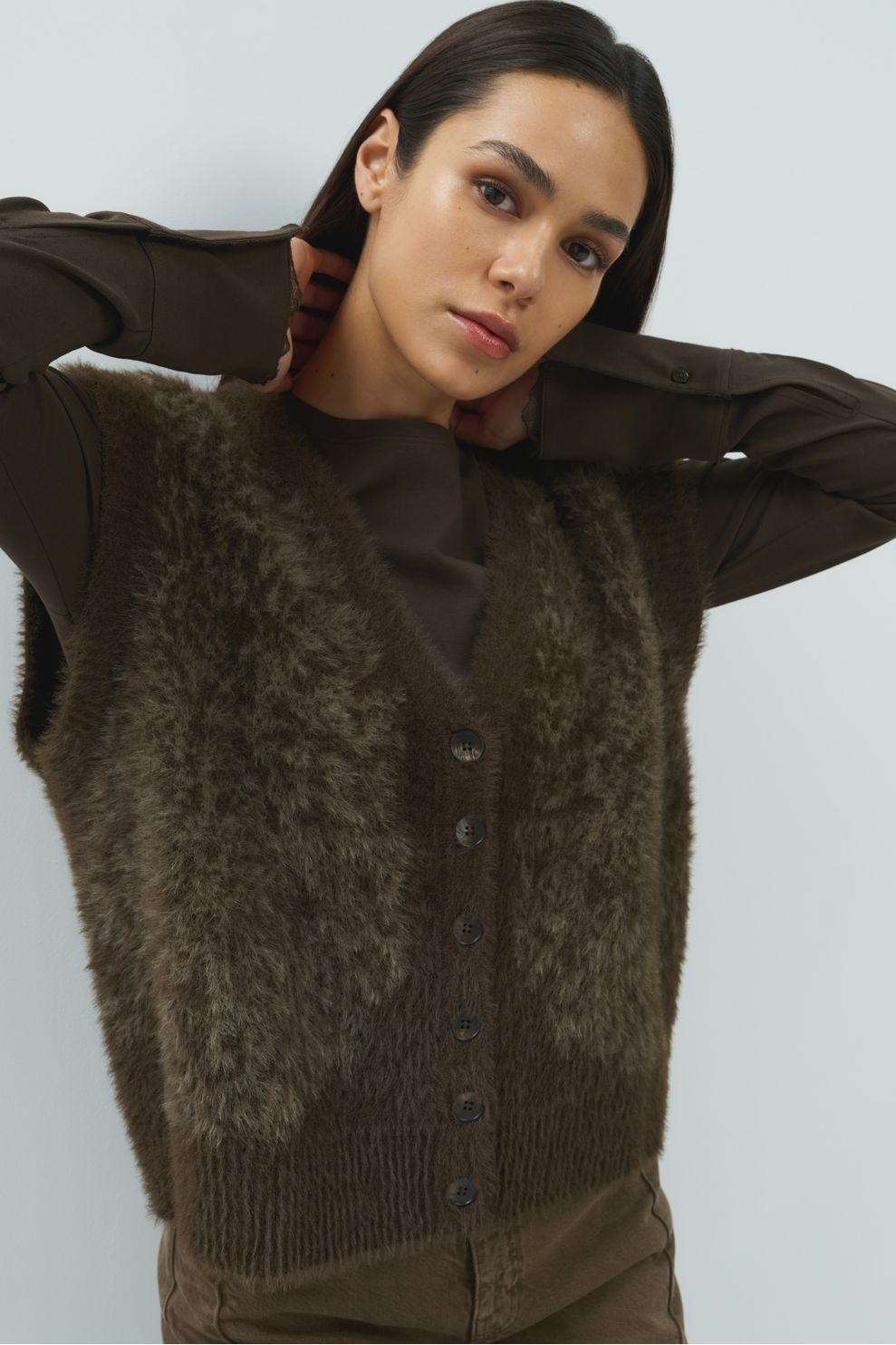 Brown fuzzy sleeveless cardigan vest with button front closure layered over brown shirt