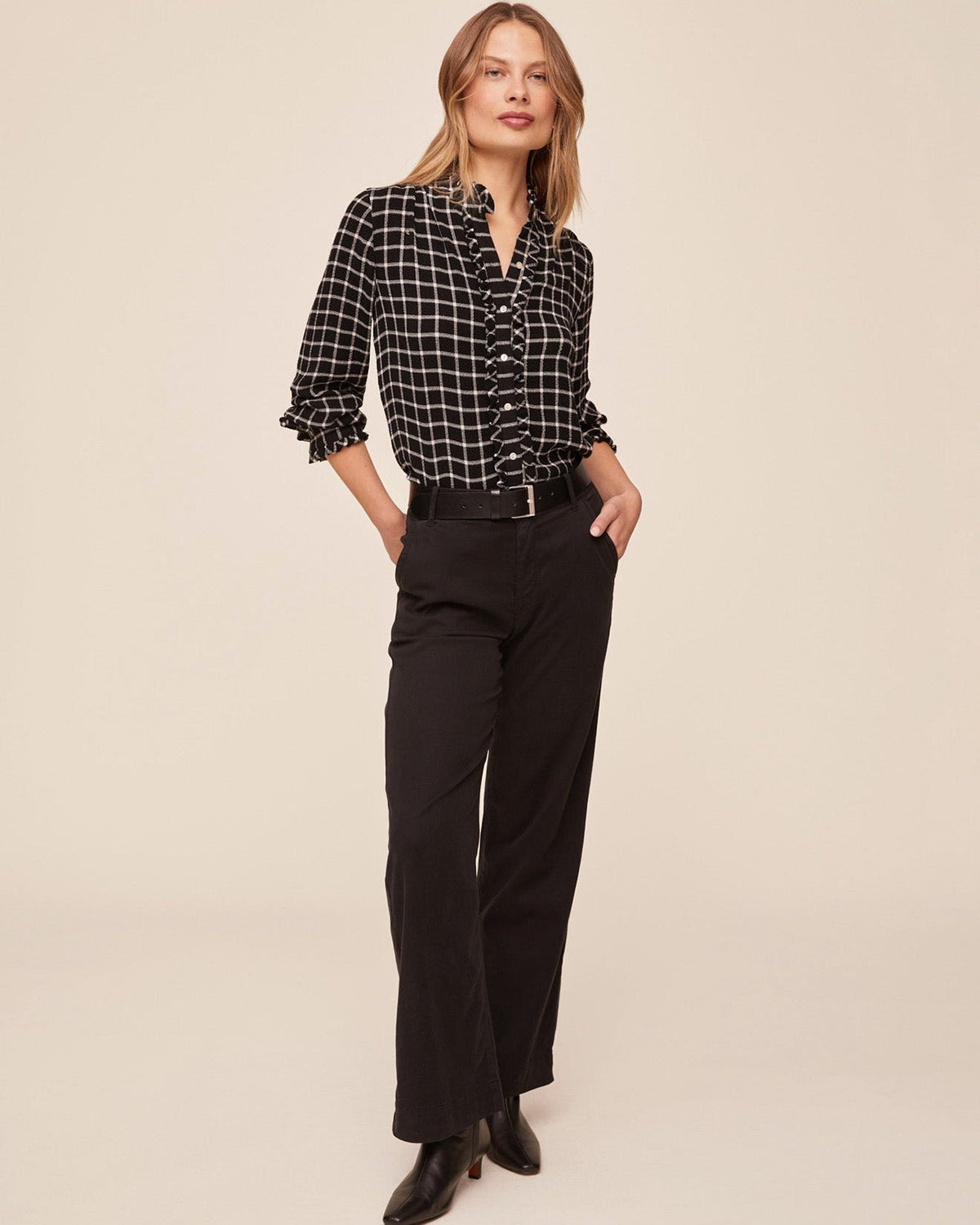 Model wearing Bella Dahl black and white plaid button-down shirt with ruffle edges and black trousers