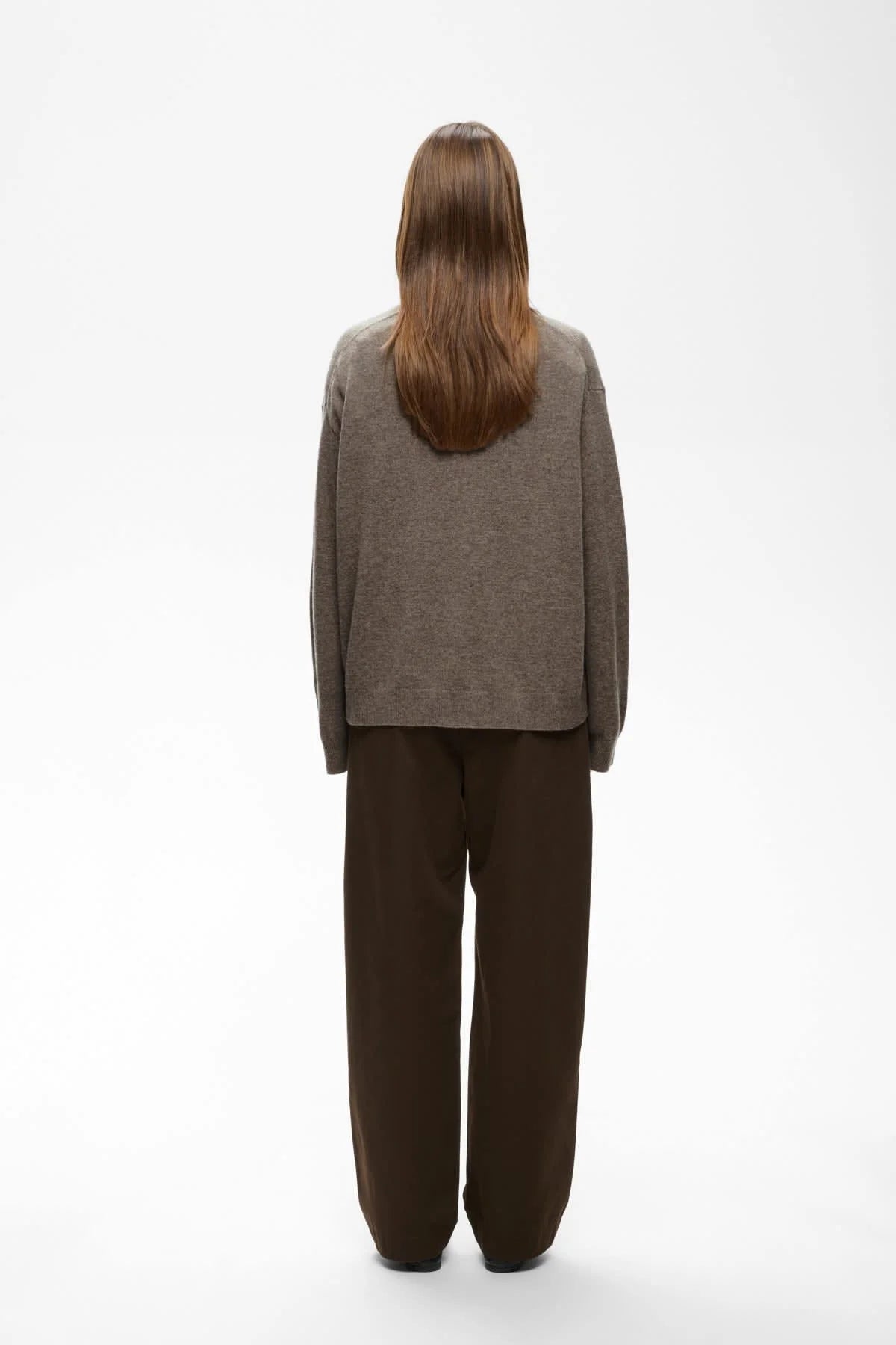 Taupe V-neck knit sweater shown from back, paired with dark brown wide-leg trousers.
