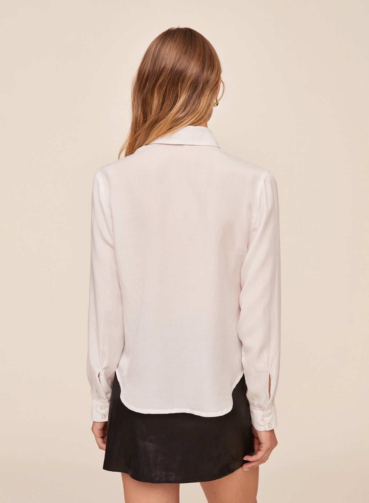 Back view of model wearing white long sleeve button-down shirt with collar and black mini skirt