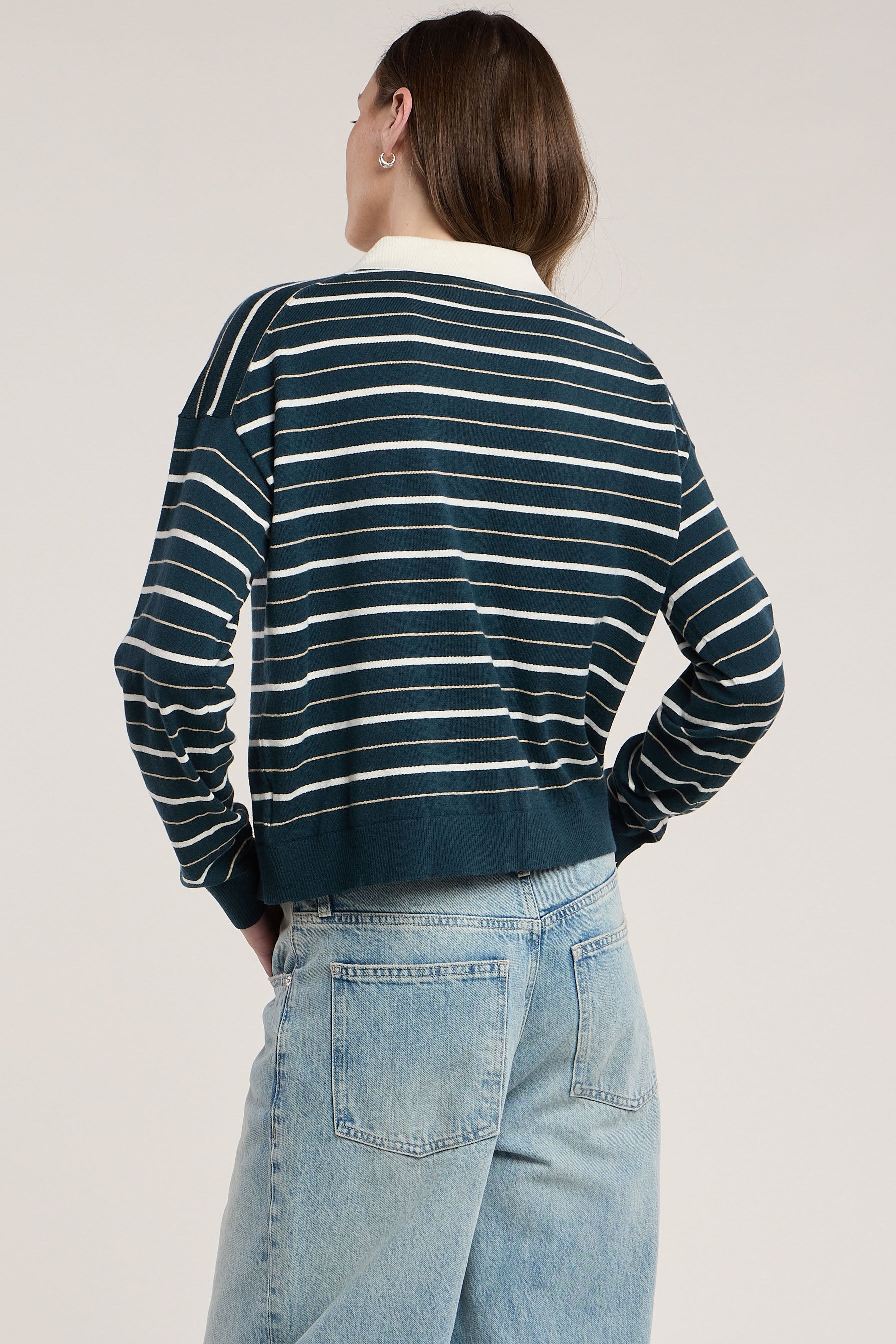 Back view of model wearing teal and cream striped sweatshirt with light wash jeans