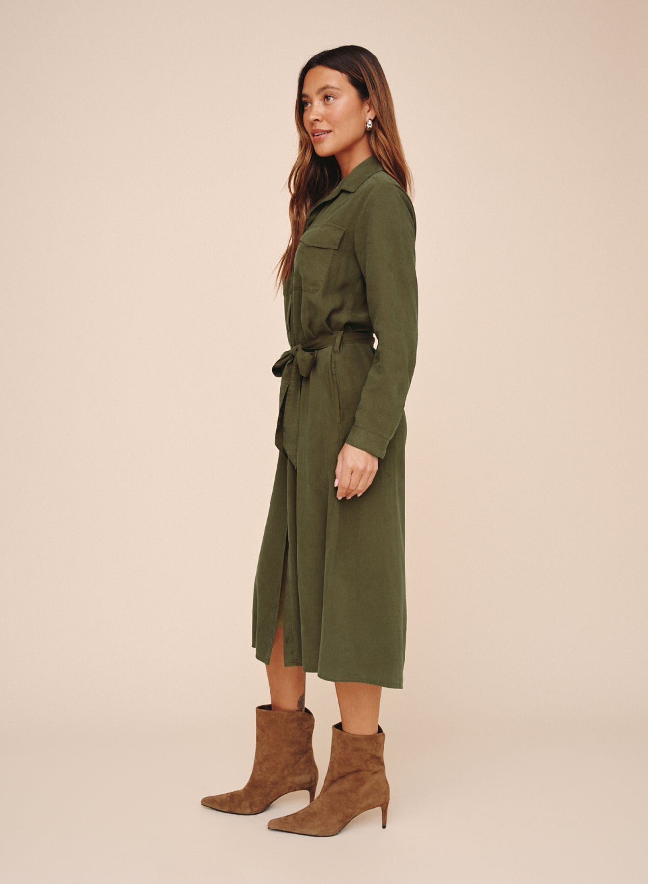Model wearing olive green belted maxi shirt dress with long sleeves and patch pocket, side view