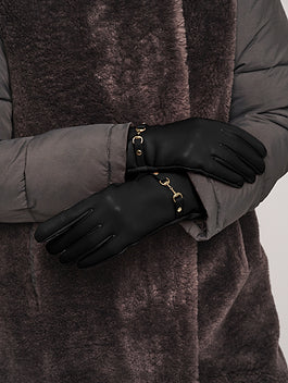 Model wearing black leather gloves with gold horsebit hardware detail, styled with winter coat