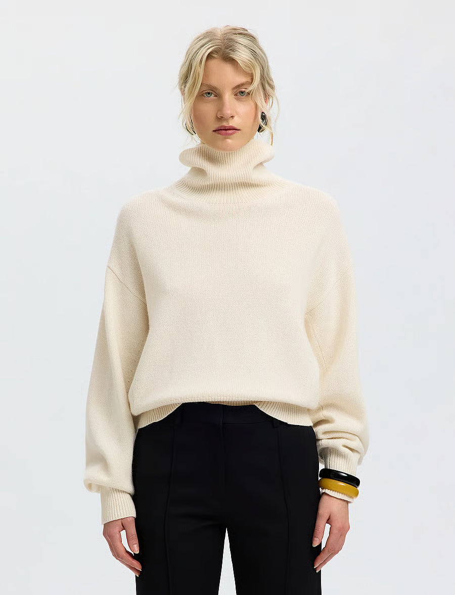 Cream oversized turtleneck knit sweater with ribbed cuffs and hem, worn with black trousers