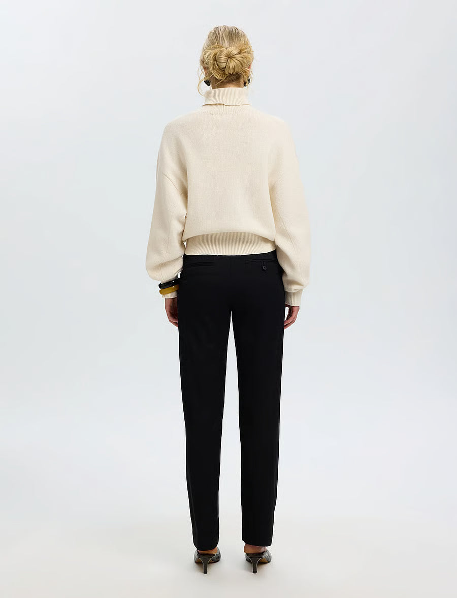 Cream turtleneck knit sweater with balloon sleeves, worn with black trousers, back view
