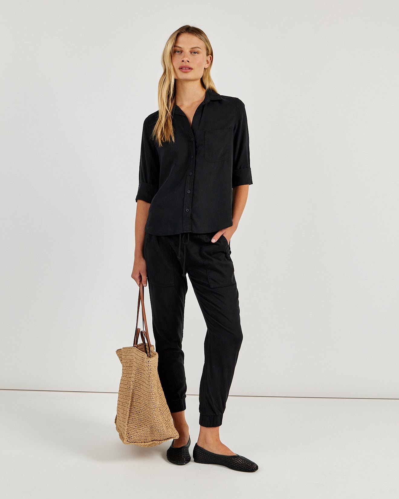 Model wearing Bella Dahl black button-down shirt with matching black jogger pants and woven tote bag.