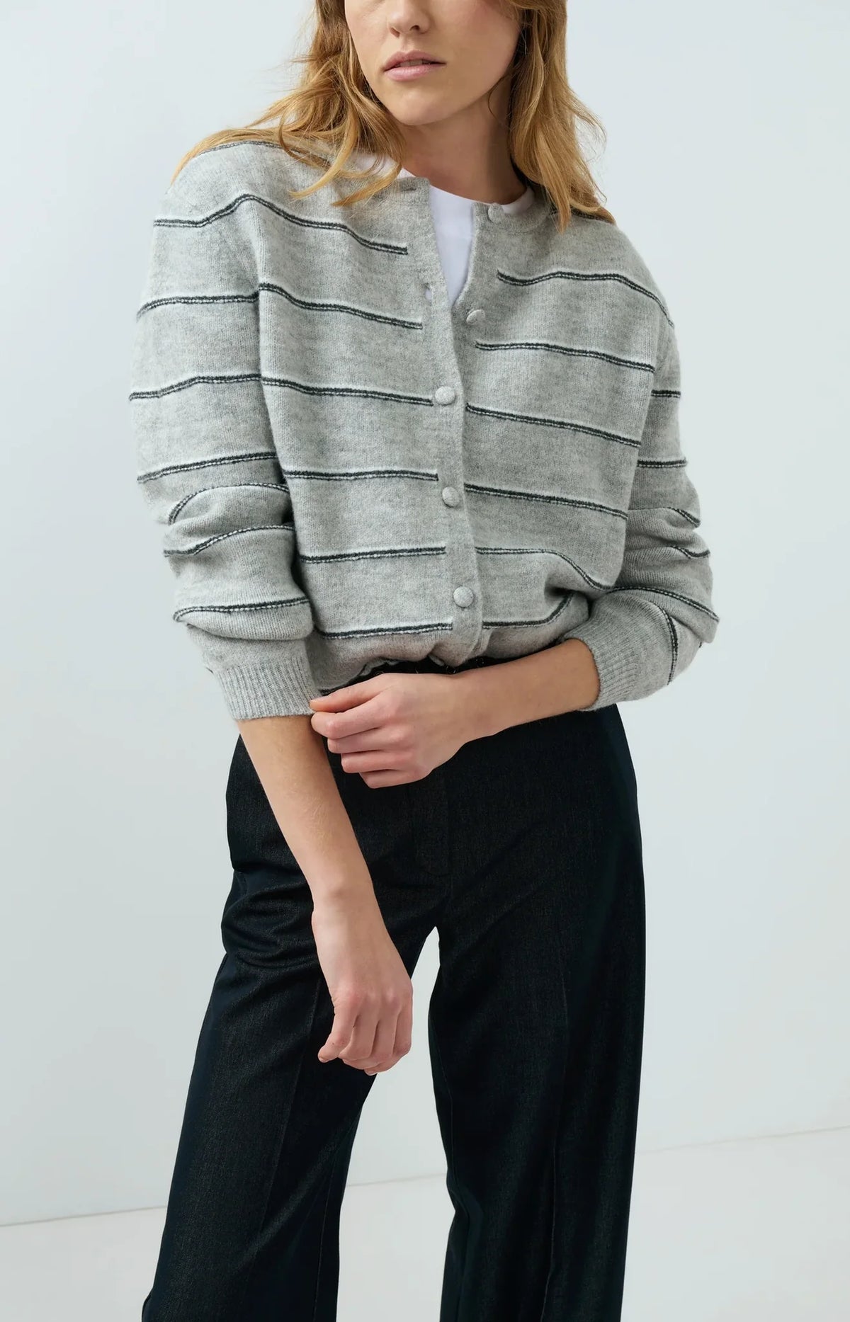 Grey knitted striped cardigan with button front and long sleeves worn with black trousers