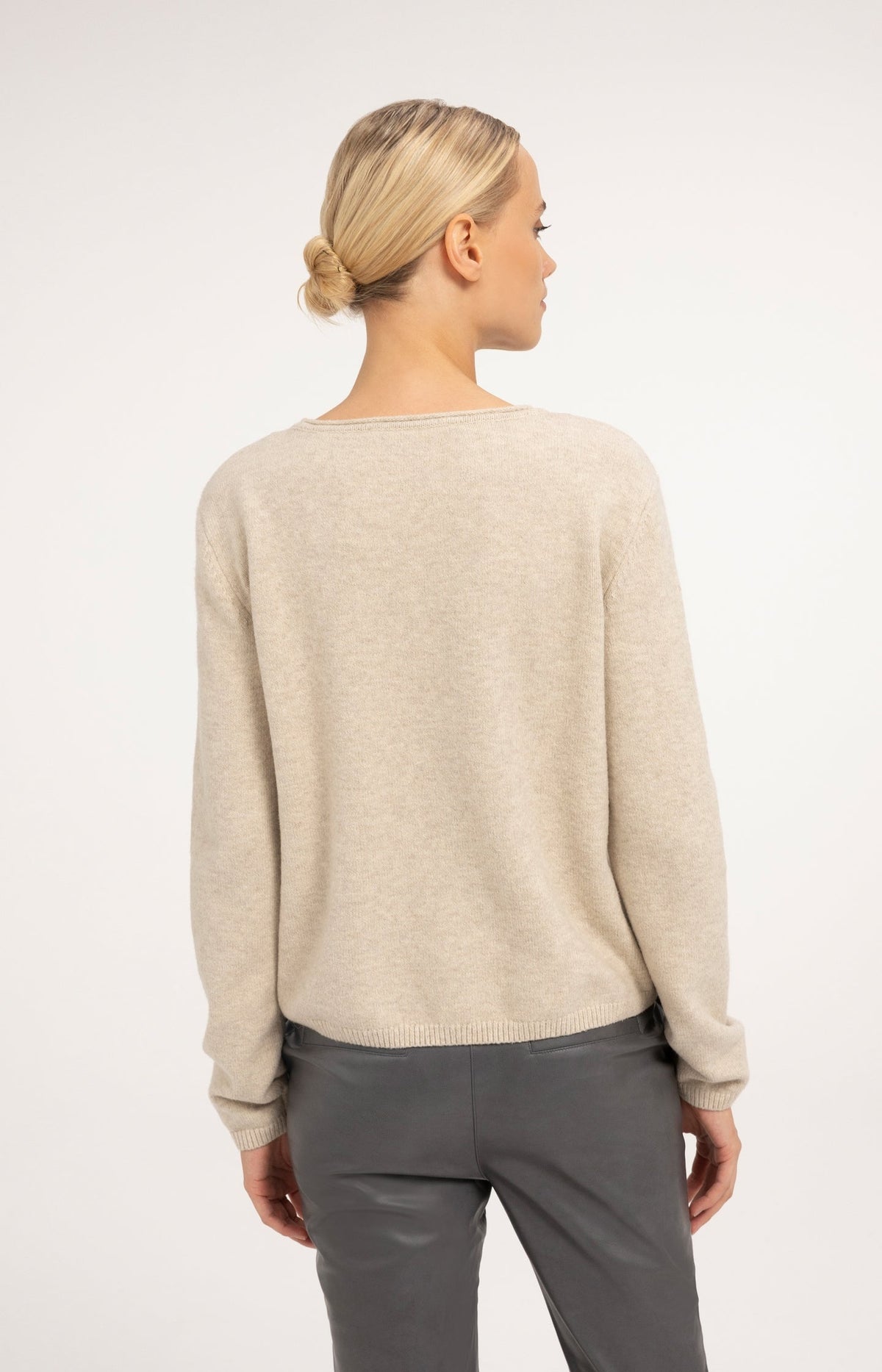 Back view of woman wearing a light beige knit sweater with gray trousers
