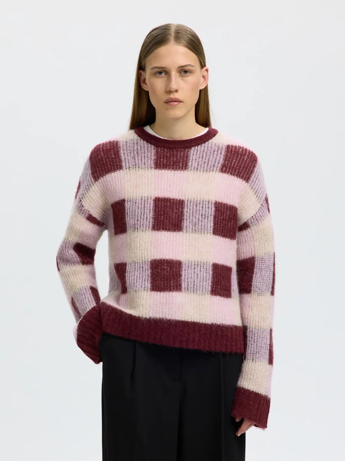 Model wearing SELECTED SLWLULU loose crew neck knit sweater in burgundy and pink checkerboard pattern