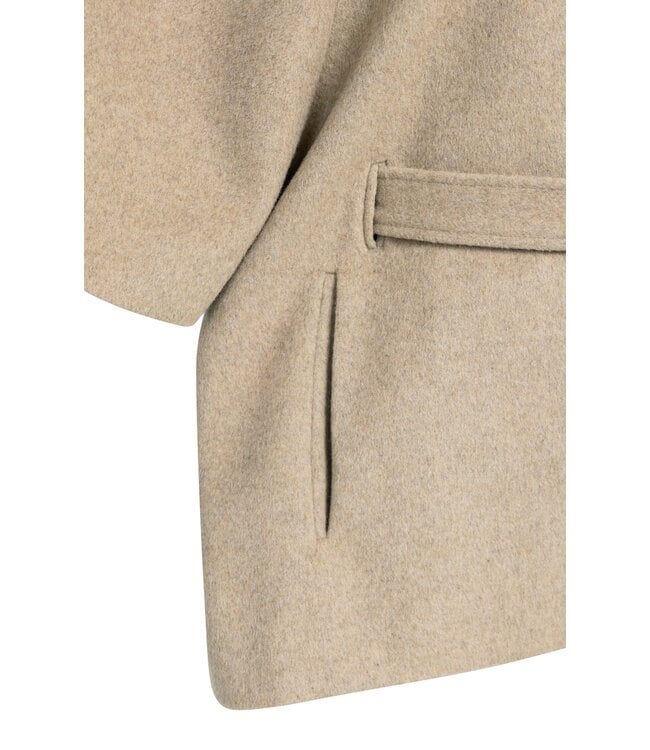 Close-up detail of beige wool poncho jacket showing belt loop and welt pocket construction