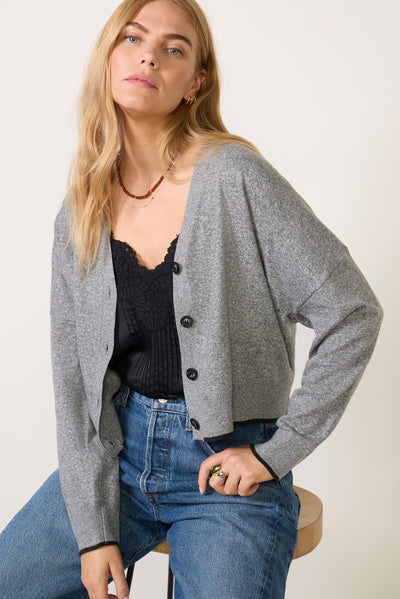 Grey cropped button-front cardigan with black trim, worn over black cami with jeans
