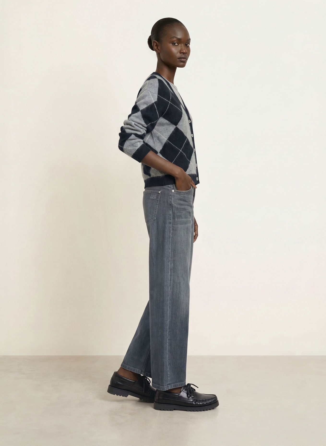 Wide-leg grey washed jeans styled with argyle cardigan and black loafers, side view