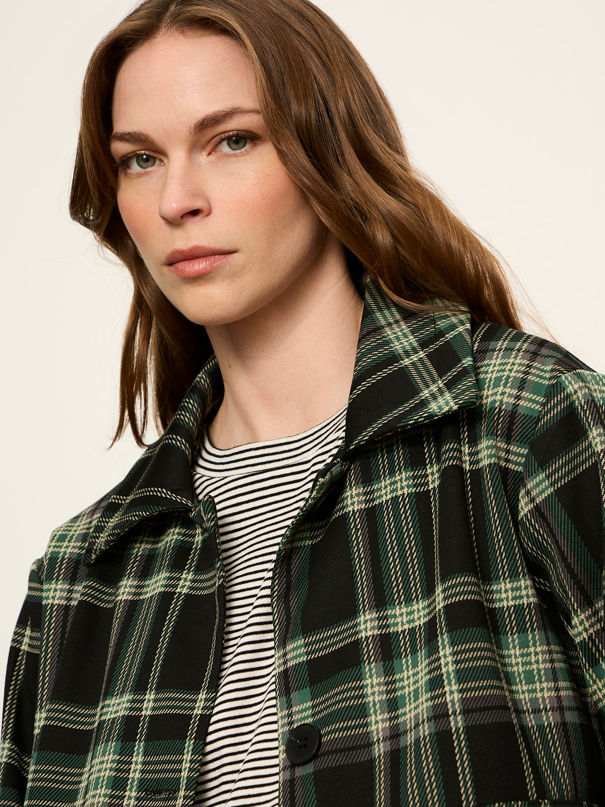 Close-up detail shot of model wearing green and black plaid jacket over striped top.