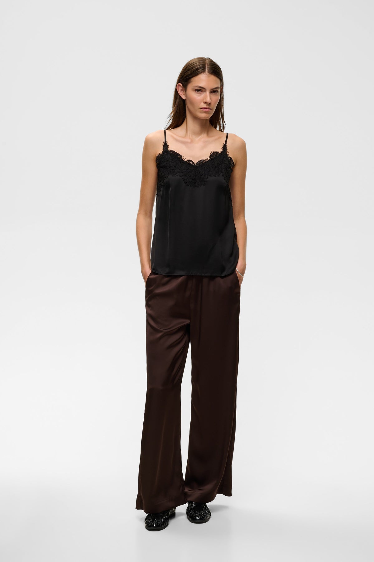 Model wearing black satin camisole with lace trim neckline and spaghetti straps, front view